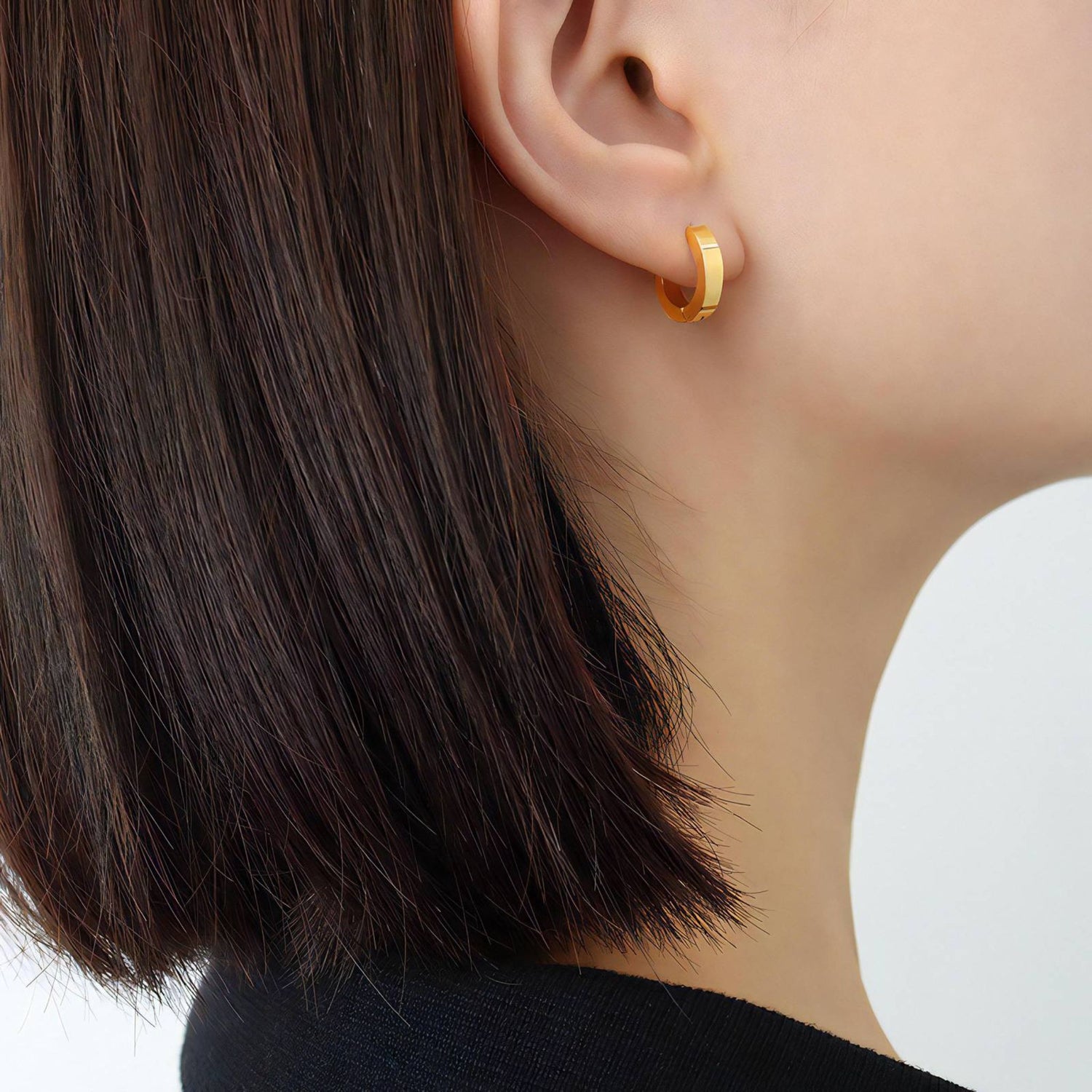Gold hoop earring worn by a person with dark hair on a neutral background